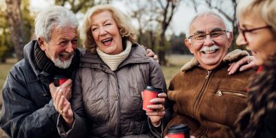 elderly people standing outside laughing and drinking coffee